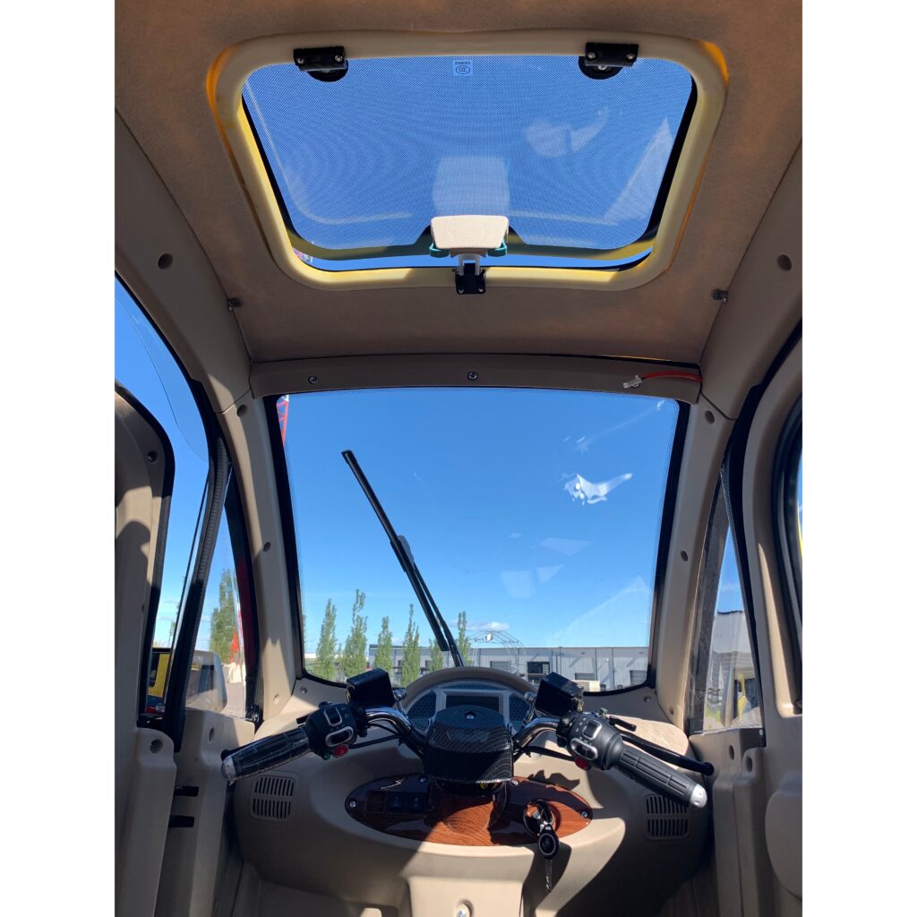 Driver's view inside a GIO Golf fully enclosed mobility scooter, showing the steering controls, dashboard, and a large front window.