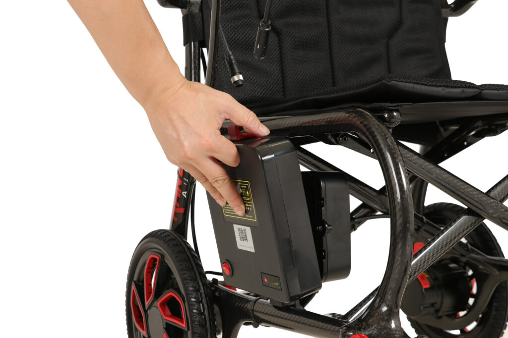 Porto Mobility Ranger Aero folding power wheelchair, hand holding the side mounted battery pack under the seat